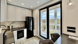Una cocina moderna con un refrigerador negro, armarios blancos y un amplio ventanal con vistas al exterior.