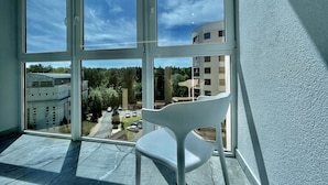 Una habitación con un amplio ventanal, una silla blanca y vistas a un edificio y árboles.