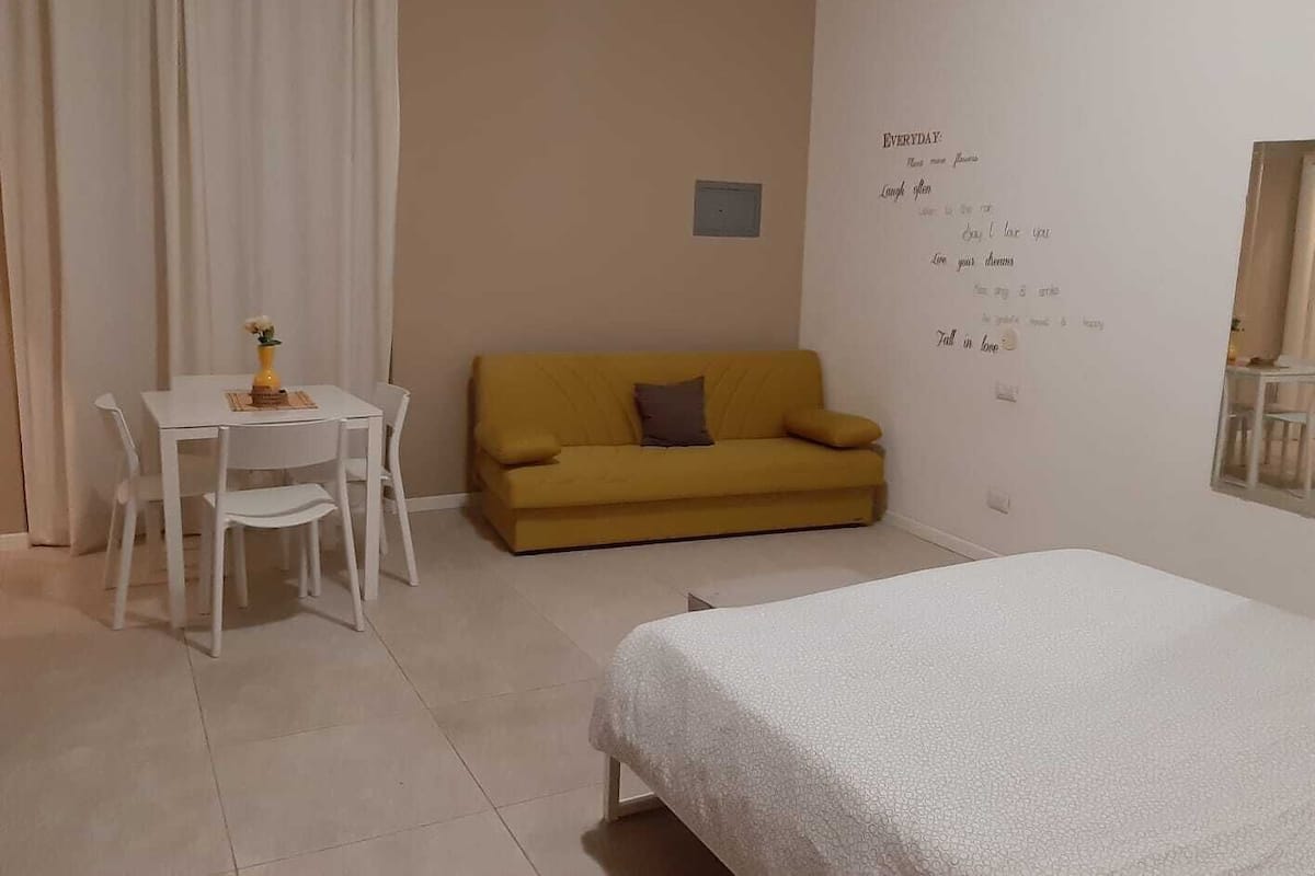 A room with a bed, a yellow sofa, a white table with chairs, and a wall with motivational quotes.
