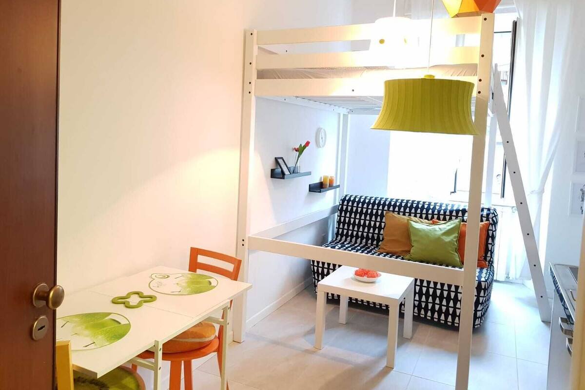 A child's bunk bed with a ladder, a small table with a green placemat, and a sofa with patterned cushions.