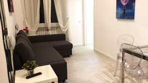 Una sala de estar moderna con un sofá seccional negro, una mesita blanca con un control remoto y una mesa de comedor de vidrio con sillas.