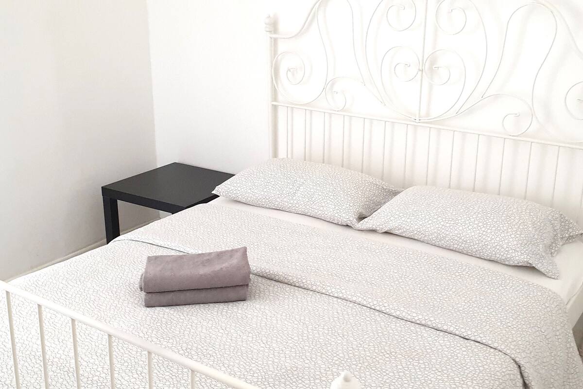 A neatly made bed with a white headboard and a small black nightstand beside it.