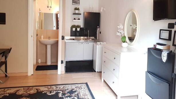 Cocina compacta con lavabo, estufa y armarios, un pequeño comedor con una silla, y un espejo grande.