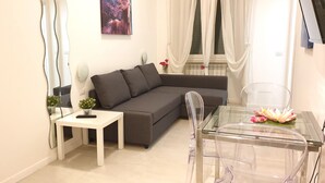 Una sala moderna con un sofá gris, una mesita auxiliar blanca y una mesa de comedor de cristal.