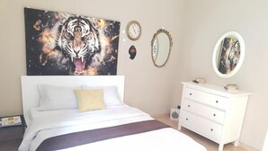 Un dormitorio con una cama, un aparador blanco, dos relojes de pared y un cuadro enmarcado.