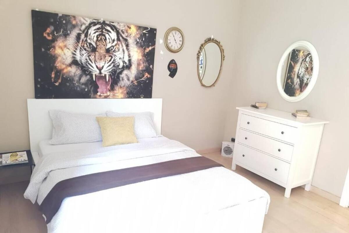 A bedroom with a bed, a white dresser, two wall clocks, and a framed picture.