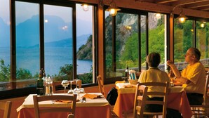 A dining area with large windows overlooking a scenic view of mountains and a body of water. - Hotel Baitone (Malcesine)