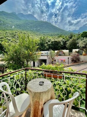 A balcony with a table and chairs, overlooking a mountainous landscape with greenery and buildings. - Hotel Baitone (Malcesine)