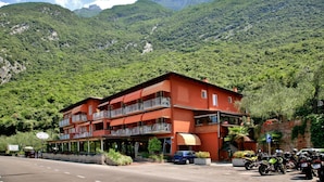 A multi-story hotel with balconies, a parking area, and a mountain backdrop. - Hotel Baitone (Malcesine)