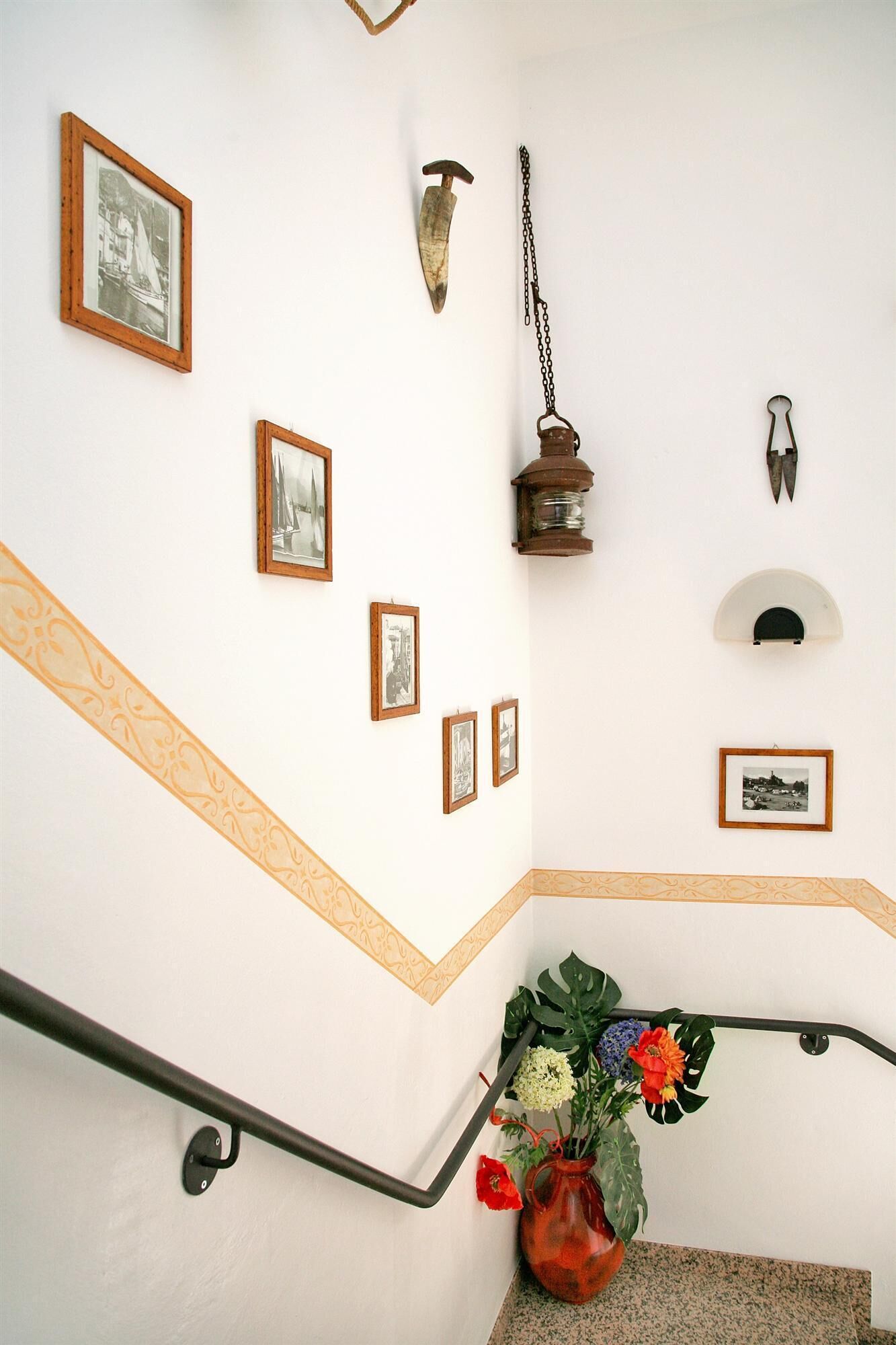 Una escalera con barandilla, un jarrón con flores y varias fotografías enmarcadas en la pared.