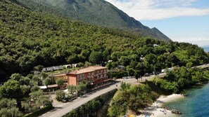 A coastal hotel with a red building, a beach, and a mountainous backdrop. - Hotel Baitone (Malcesine)
