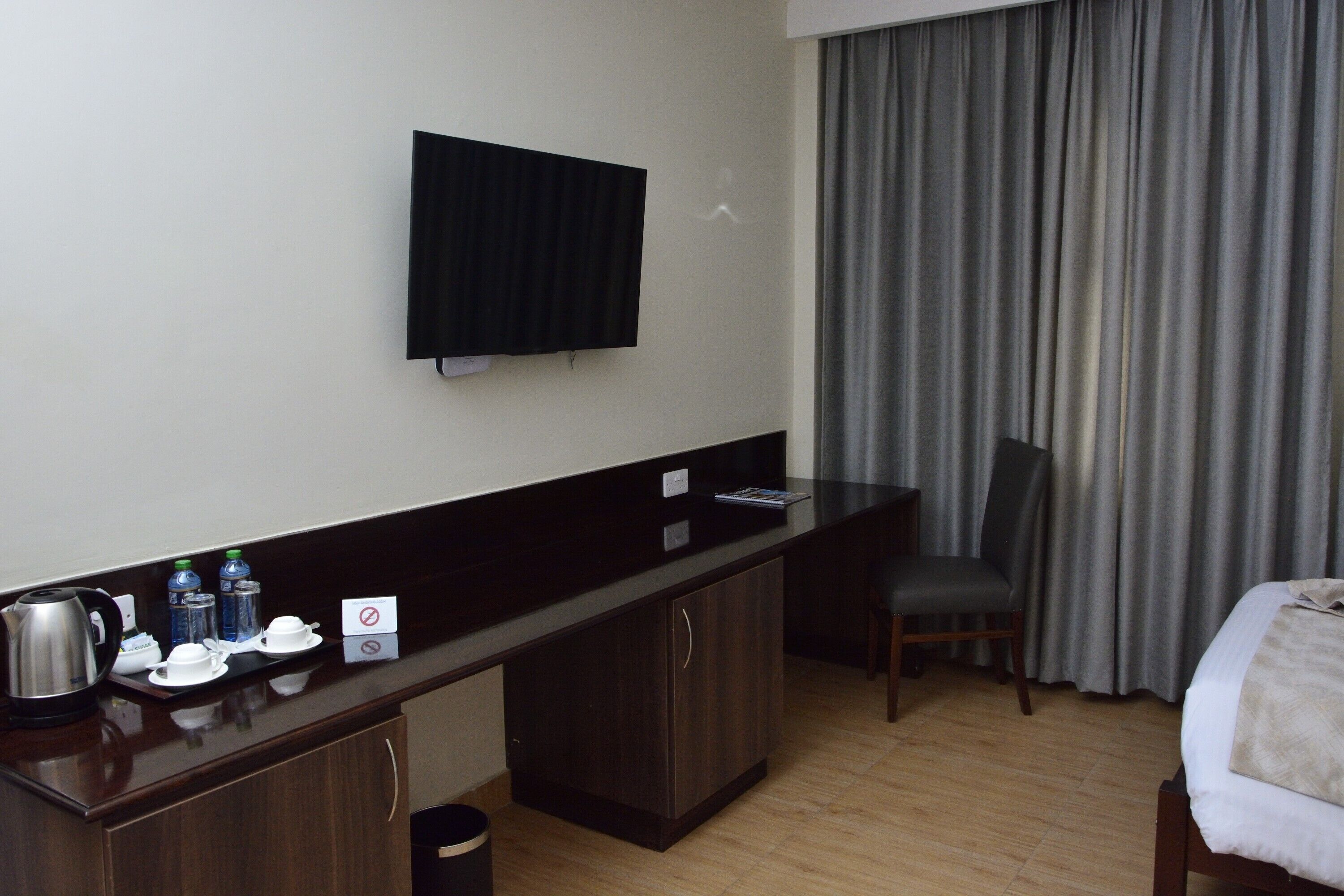 A hotel room with a wooden desk, a television, a bed, a chair, and a window with curtains.