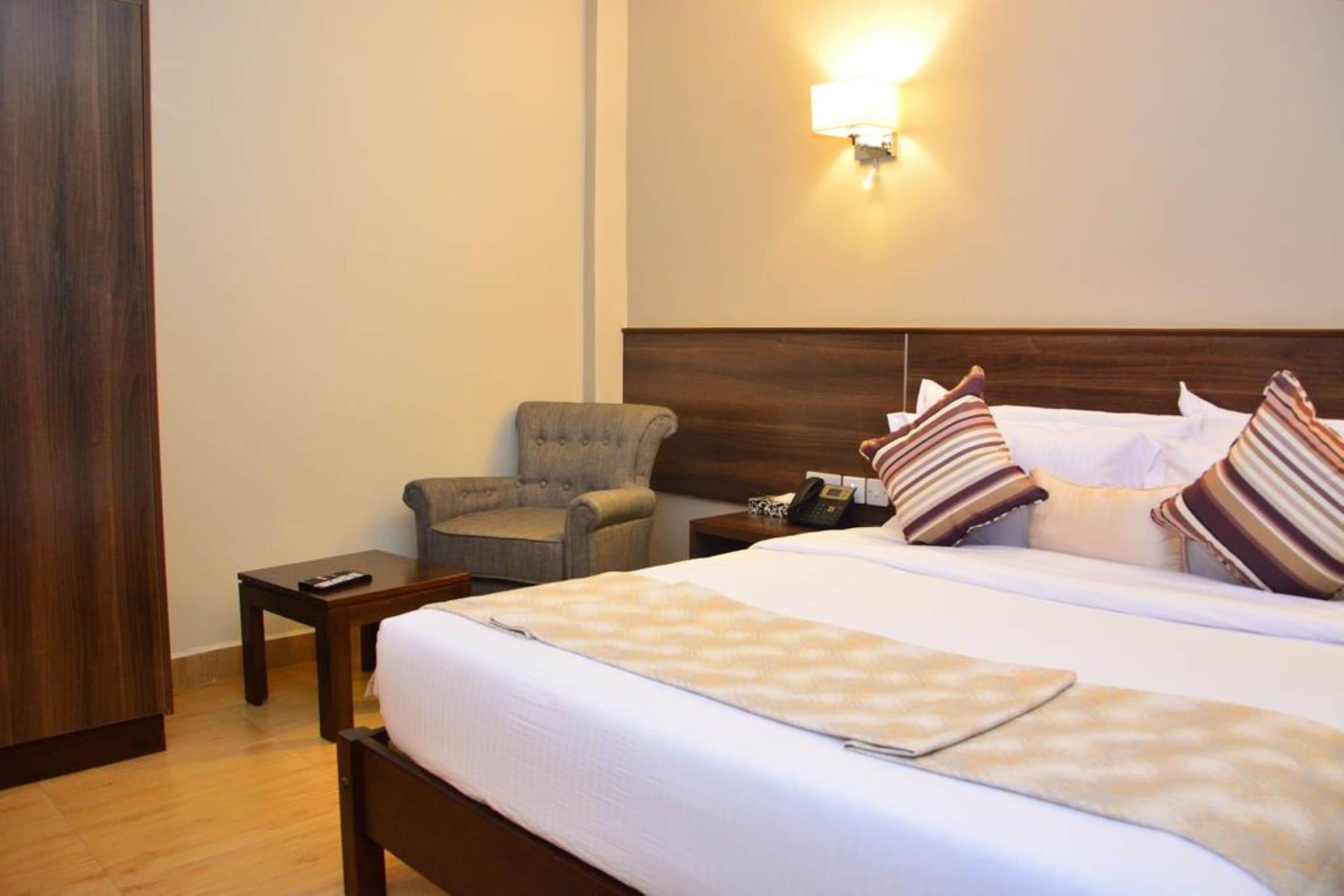 A hotel room with a large bed, a bedside table, a chair, and a wall-mounted lamp.