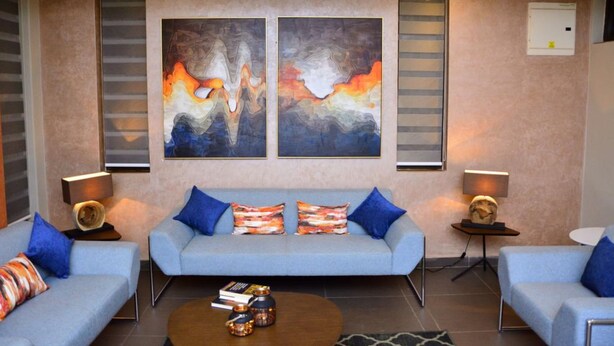 Una sala de estar moderna con un sofá azul, dos cuadros abstractos y una mesita de centro con libros y objetos decorativos.