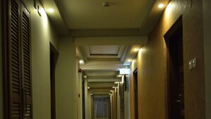 Un largo y estrecho pasillo de hotel con puertas a ambos lados, iluminación empotrada y suelo de baldosas.