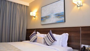 Una habitación de hotel con una cama grande, cabecera, un cuadro en la pared y dos lámparas de pared.