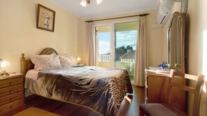 Un dormitorio con cama, mesita de noche, cómoda, silla y ventana con cortinas.