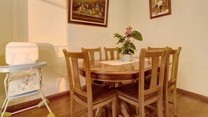 Un comedor con una mesa redonda de madera, seis sillas, una trona y dos cuadros en la pared.
