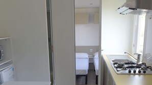 A compact kitchen with a dining area, a bed in the adjacent room, and a small kitchenette. - Camping Alpino (Malcesine)