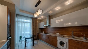 A modern kitchen with a built-in washing machine, a dining area with a glass table, and a large window with sheer curtains. - HOME APART Storozhovskaya str. 6 (Minsk)