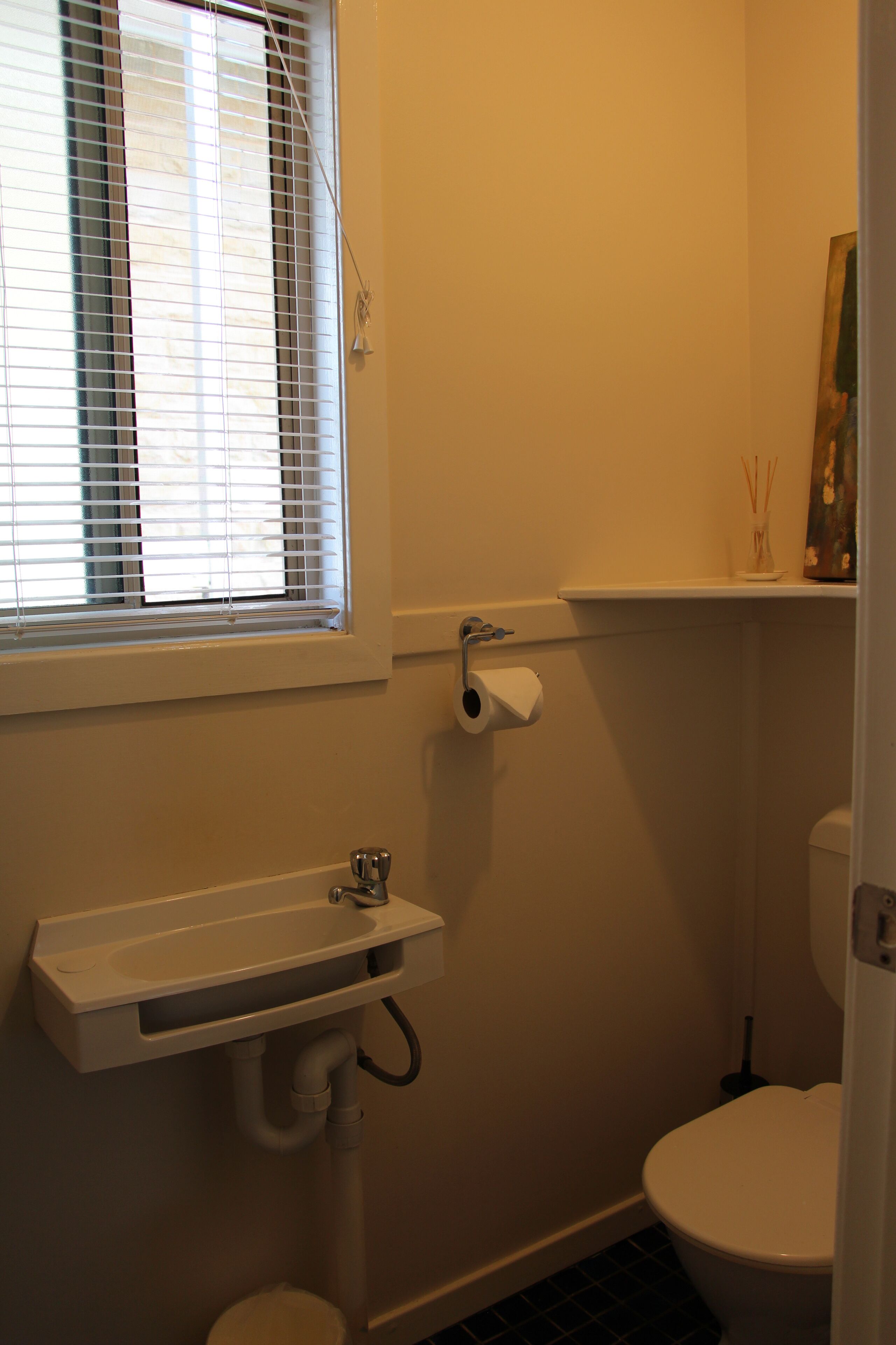 Ein Badezimmer mit Toilette, Waschbecken, einem Fenster mit Jalousien und einem Toilettenpapierhalter.