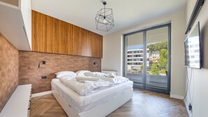 Une chambre moderne avec un grand lit, un mur recouvert de panneaux en bois et une vue dégagée sur l’extérieur grâce à une porte-fenêtre coulissante.