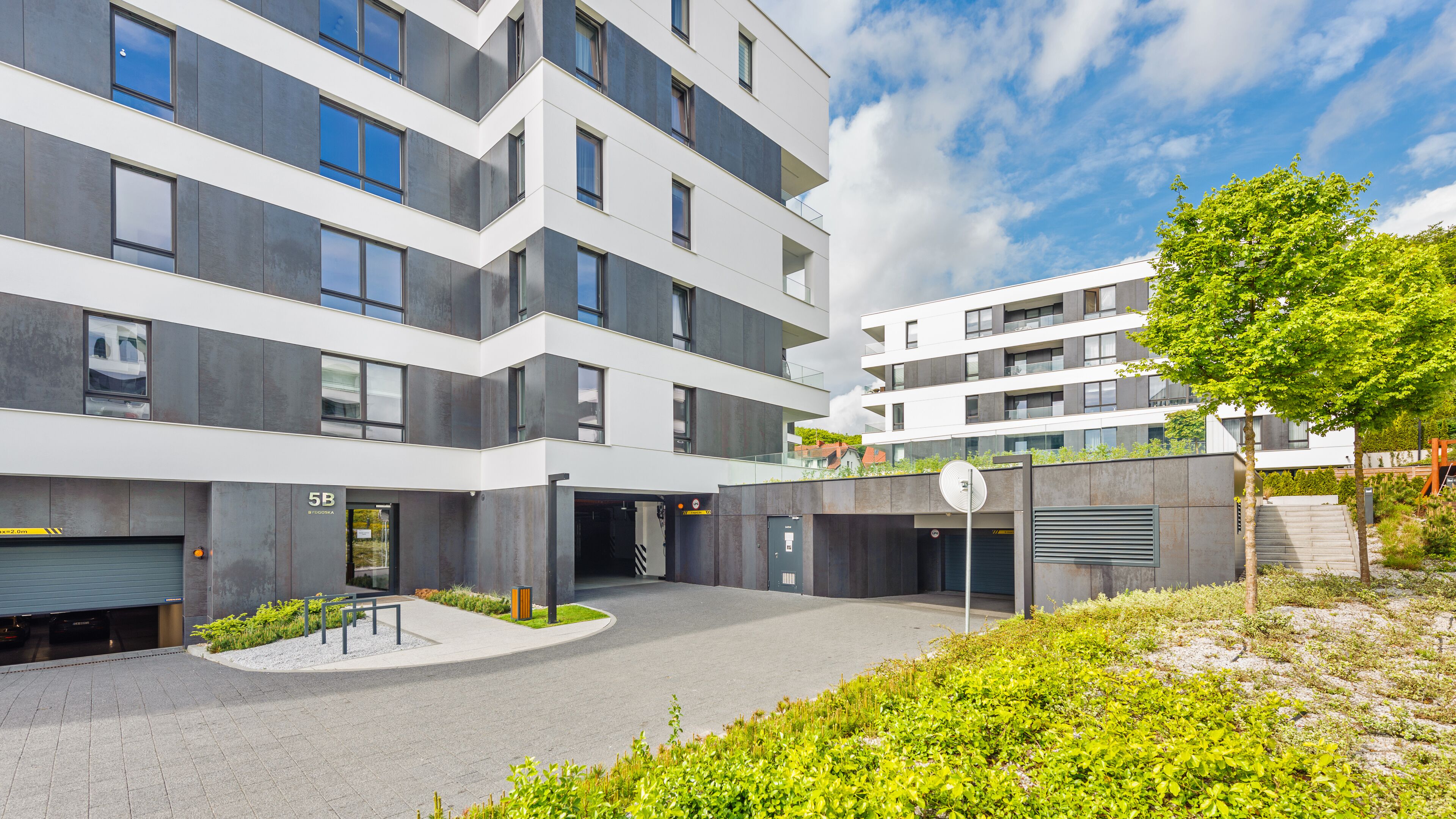 Een modern meerlaags gebouw met een binnentuin, met een combinatie van balkons en grote ramen, en een klein tuintje met een bankje.