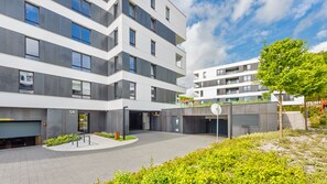 A modern multi-story building with a courtyard, featuring a mix of balconies and large windows, and a small garden area with a bench. - Sun & Snow Silva (Gdynia)