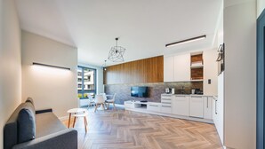 Une cuisine moderne avec un parquet disposé en chevrons, un téléviseur encastré et des meubles de cuisine blancs.
