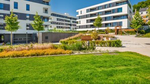 Un immeuble d’appartements moderne, doté de plusieurs étages, de grandes fenêtres et d’un espace paysager bien entretenu, avec pelouse et arbustes.
