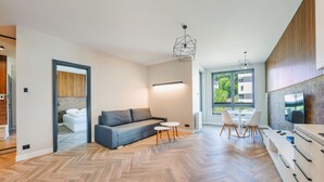 Un salon moderne avec un canapé, une table à manger et des chaises. Un téléviseur est fixé au mur et un luminaire est suspendu au plafond.
