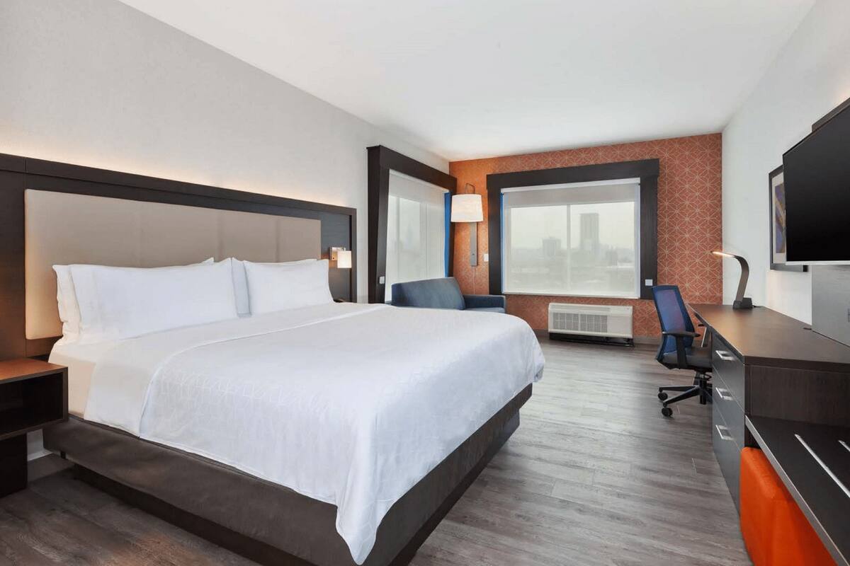 Ein modernes Hotelzimmer mit einem großen Bett, einem Schreibtisch, einem Stuhl und einem Fernseher.