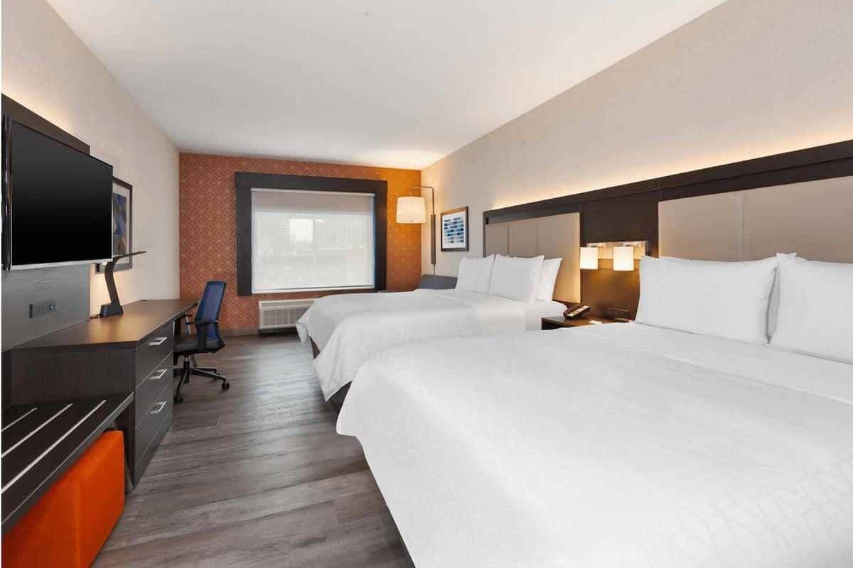 Ein Hotelzimmer mit zwei Betten, einem Schreibtisch mit Fernseher und einem großen Fenster.