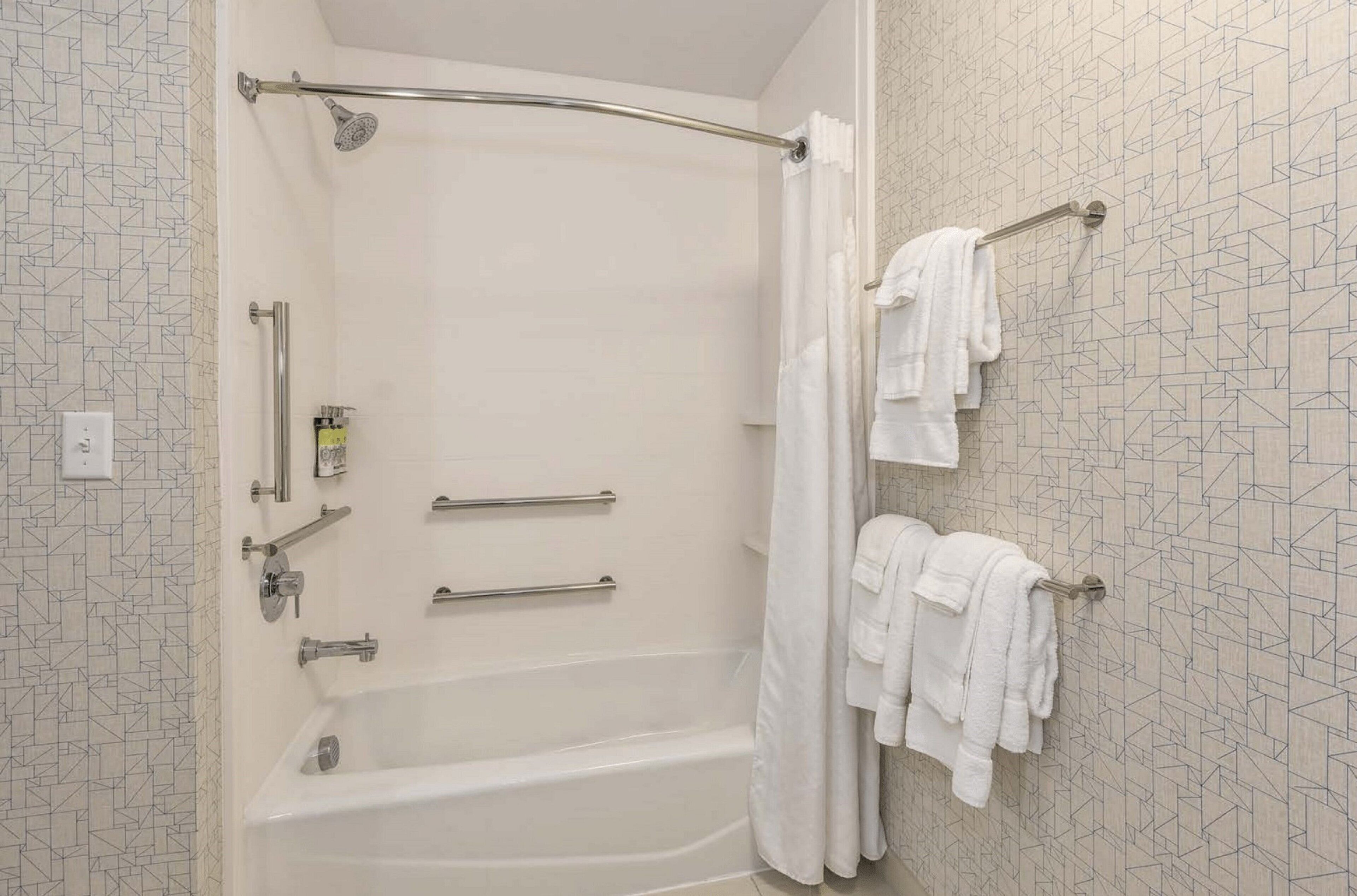 Ein Badezimmer mit einer Badewanne, Haltegriffen, einer Duschvorhang und Handtüchern auf einem Ablagekorb.