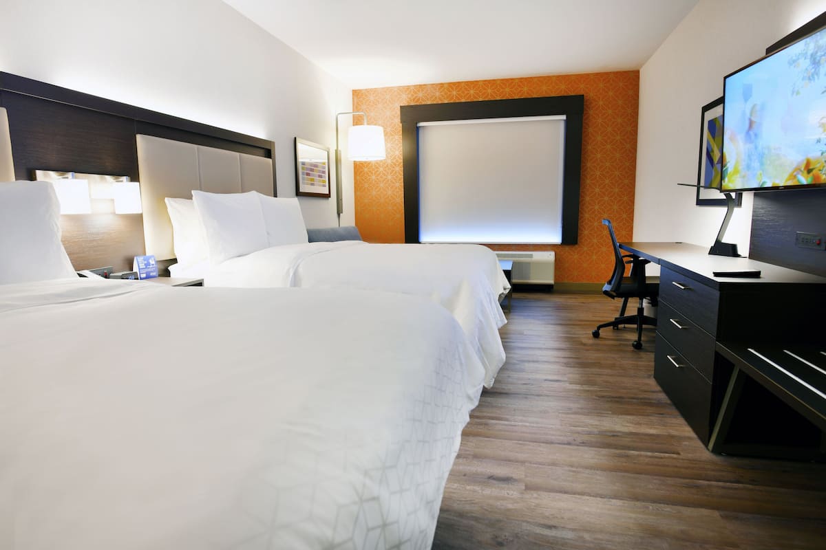 Ein Hotelzimmer mit zwei Betten, einem Schreibtisch, einem Stuhl und einem Fernseher.
