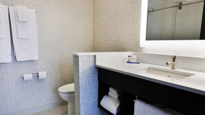 A modern bathroom with a white sink, a mirror, and a toilet. There are towels hanging on the wall and a roll of toilet paper.