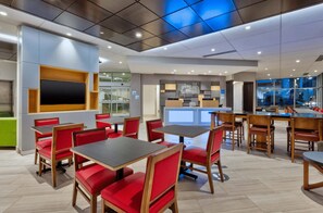 A modern restaurant interior with red upholstered booths and wooden tables, a large flat-screen TV mounted on the wall, and a view of the city through large windows. - Holiday Inn Express & Suites Jersey City - Holland Tunnel by IHG (Jersey City)