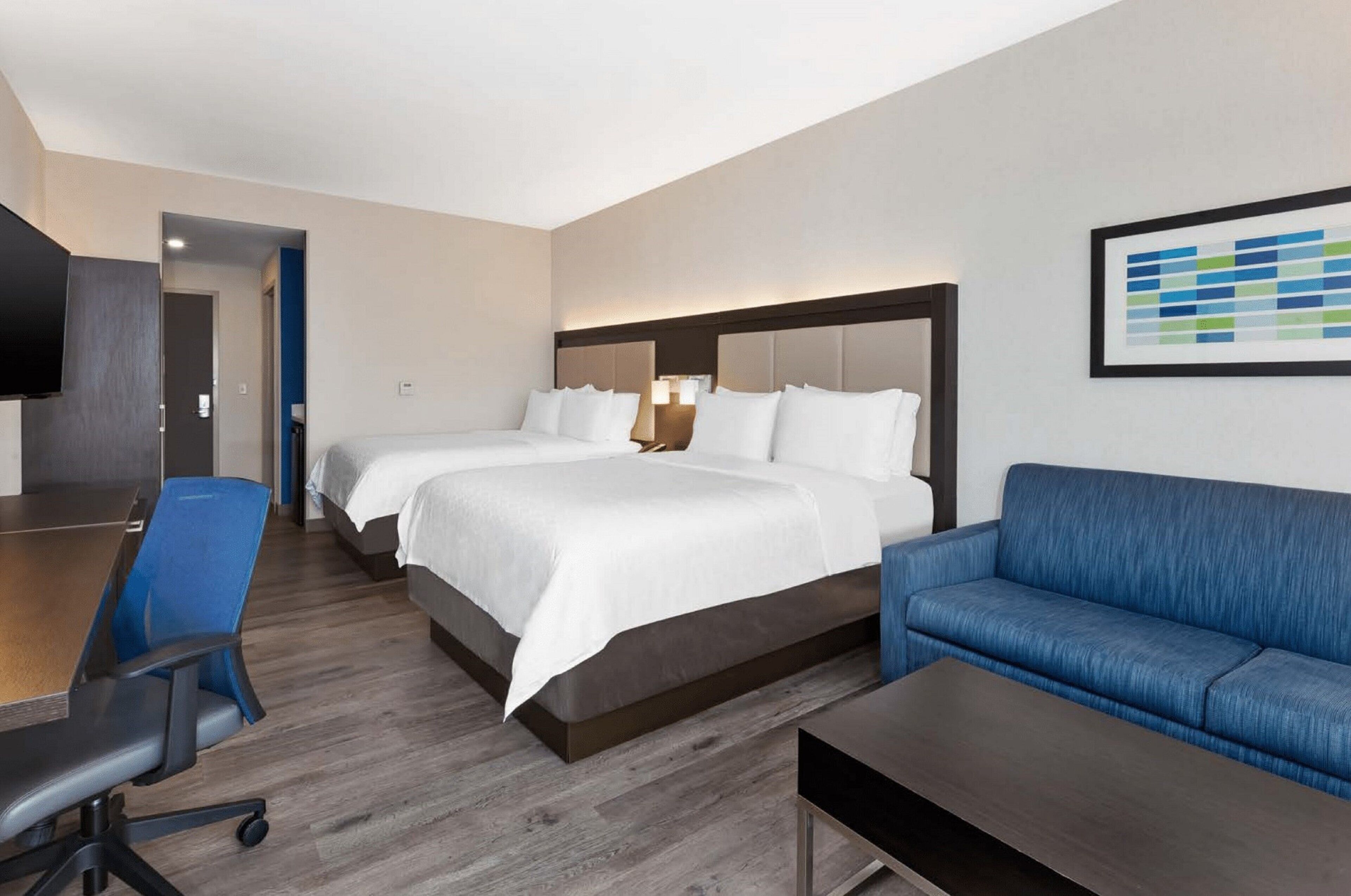 A hotel room with two beds, a desk, a blue sofa, and a flat-screen TV.