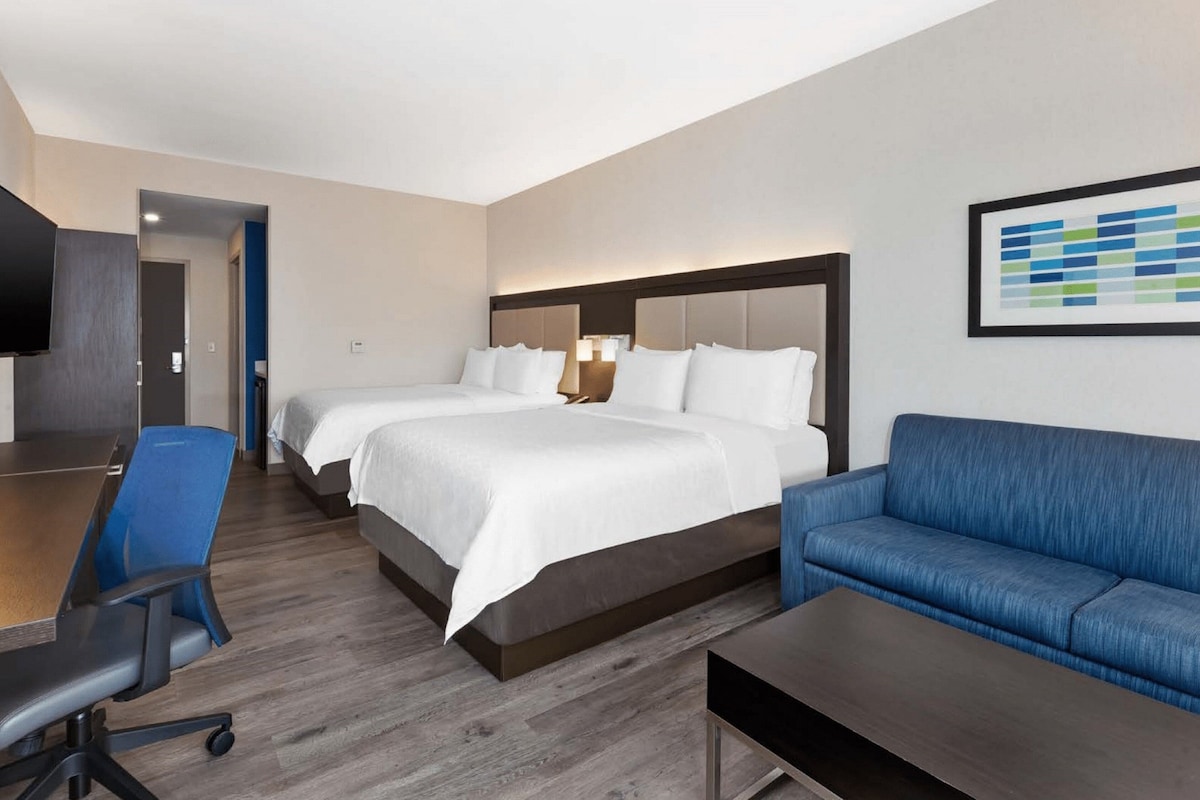 Hotellihuone, jossa on kaksi sänkyä, työpöytä, sininen sohva ja litteänäyttöinen televisio.