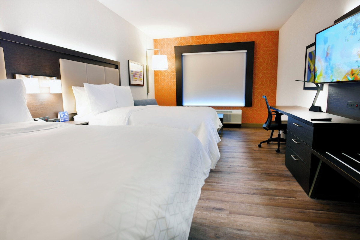 Hotellihuone, jossa on kaksi sänkyä, työpöytä, tuoli, televisio ja suuri ikkuna.