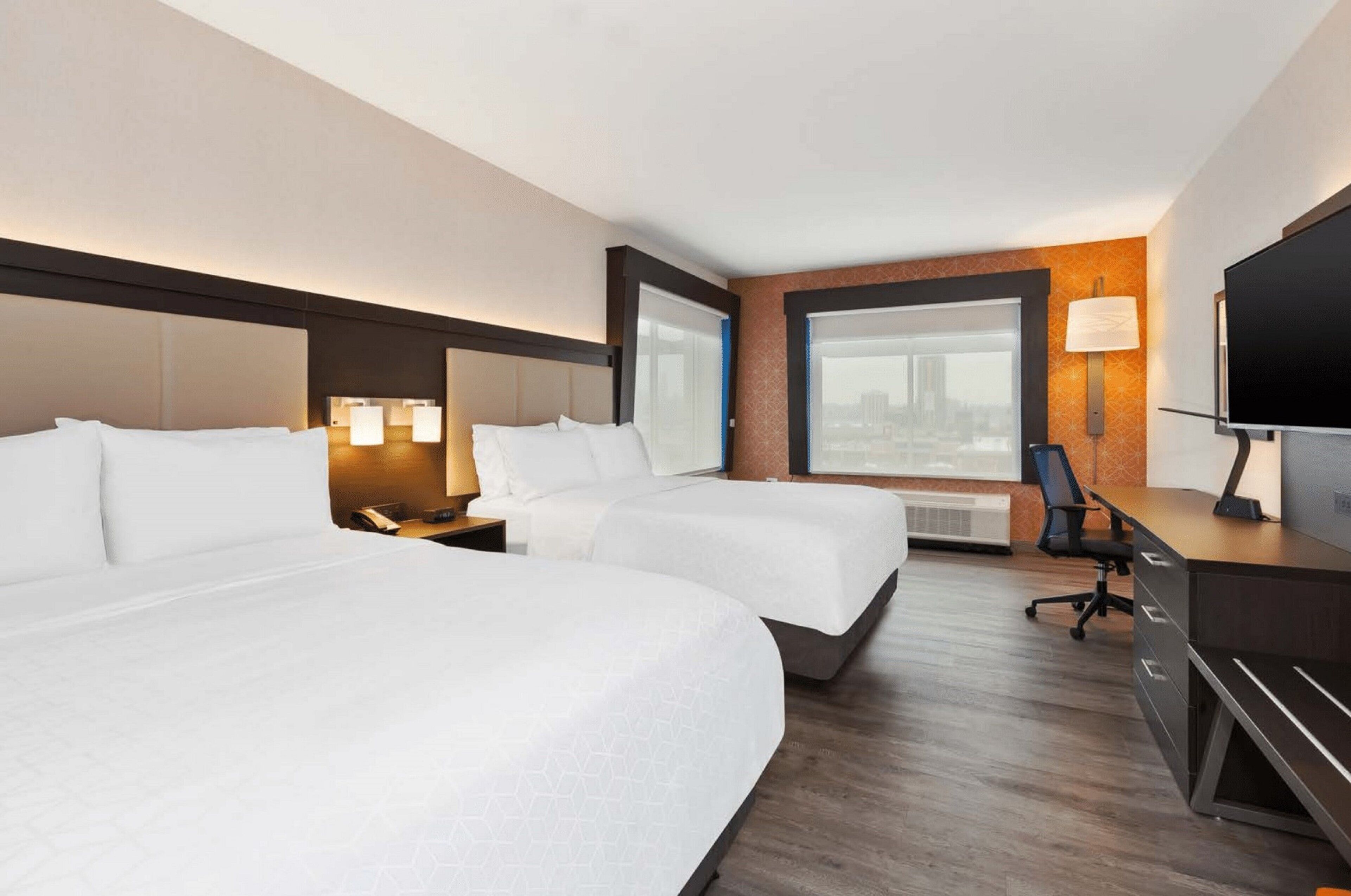 Habitación de hotel con dos camas, un escritorio con silla, televisor y ventana con vistas.