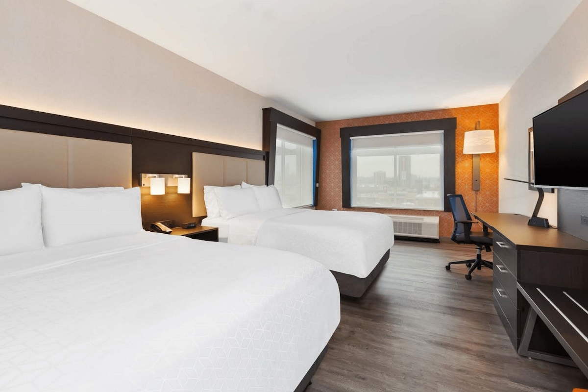 Hotellihuone, jossa on kaksi sänkyä, työpöytä tuolilla, televisio ja ikkuna, josta on näkymä.