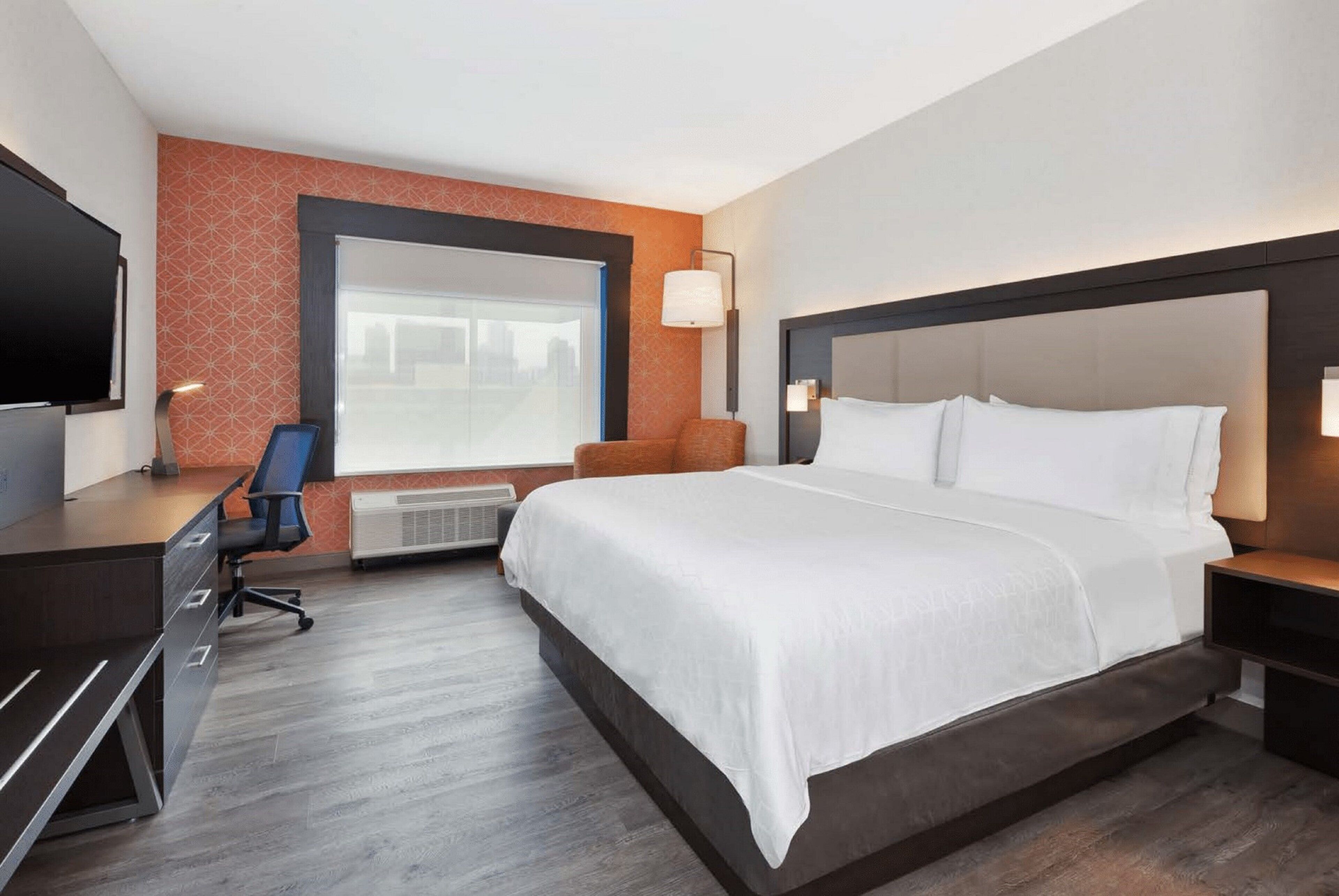 Une chambre d’hôtel avec un grand lit, un bureau, une chaise, une télévision et une fenêtre donnant sur la ville.