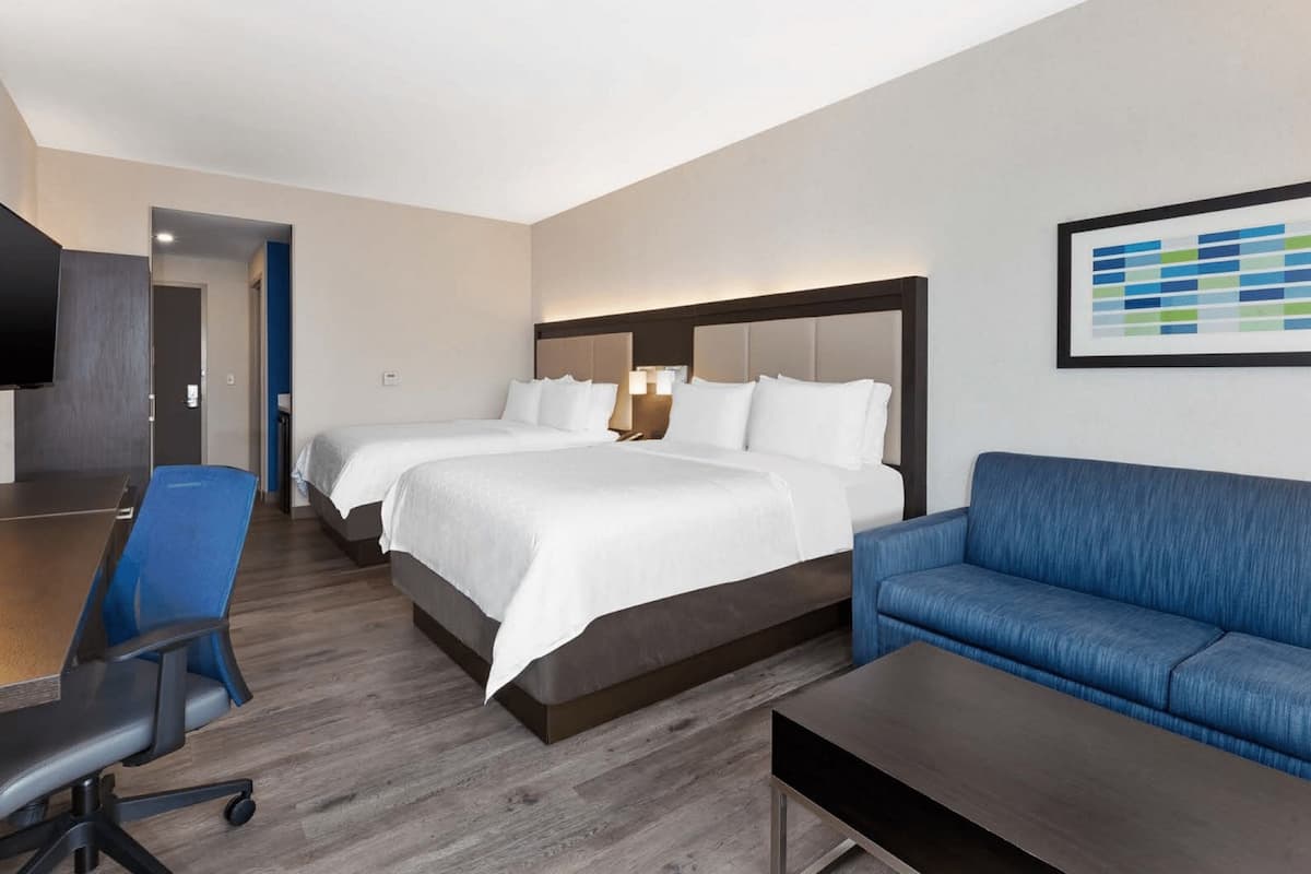 Ein Hotelzimmer mit zwei Betten, einem Schreibtisch, einem blauen Sofa und einem Flachbildfernseher.