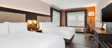 A hotel room with two beds, a desk, a chair, a TV, and a large window with a city view.