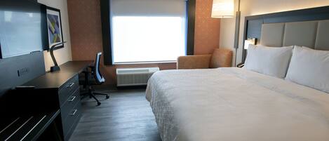 A hotel room with a large bed, a desk with a chair, a TV, and a window with blinds.