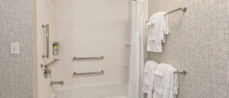 A modern bathroom with a walk-in shower, grab bars, a bathtub, and a towel rack with towels.