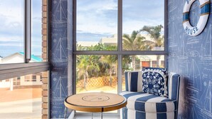 A room with a large window, a blue and white striped sofa, a round wooden table, and a life preserver on the wall. - Villa Nikos J-Bay (Jeffreys Bay)