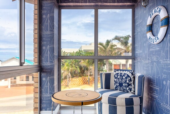 A room with a large window, a blue and white striped sofa, a round wooden table, and a life preserver on the wall.