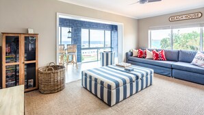 A living room with a large window, a sofa, a striped ottoman, and a bookshelf. - Villa Nikos J-Bay (Jeffreys Bay)